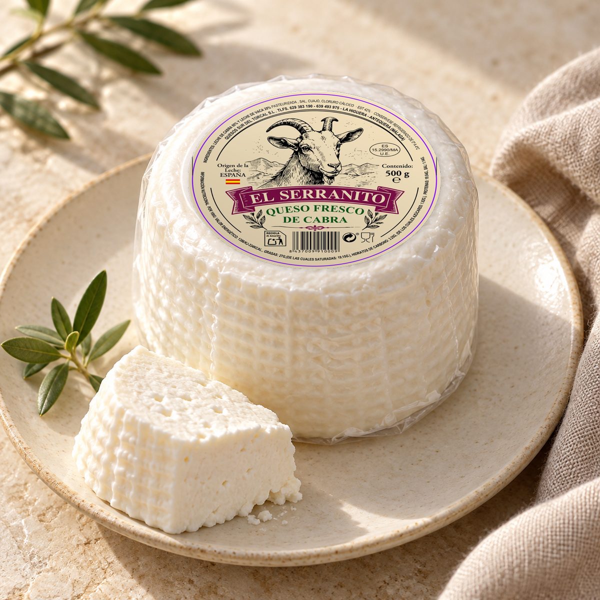 Queso fresco de cabra El Serranito sobre un plato, con una cuña cortada y ramas de olivo